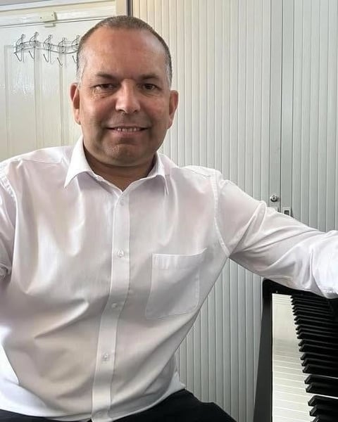 Graham Woods, music teacher, smiling at the camera in a white shirt next to a keyboard